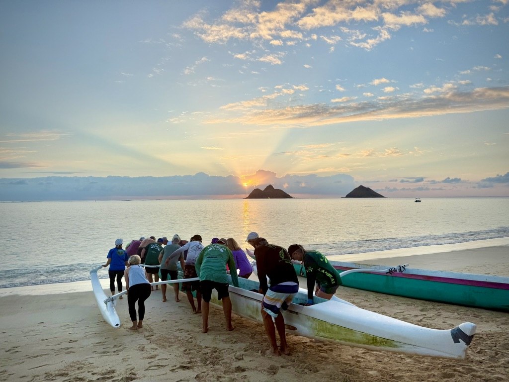 Paddlers launching an outrigger canoe from Lanikai Beach at sunrise