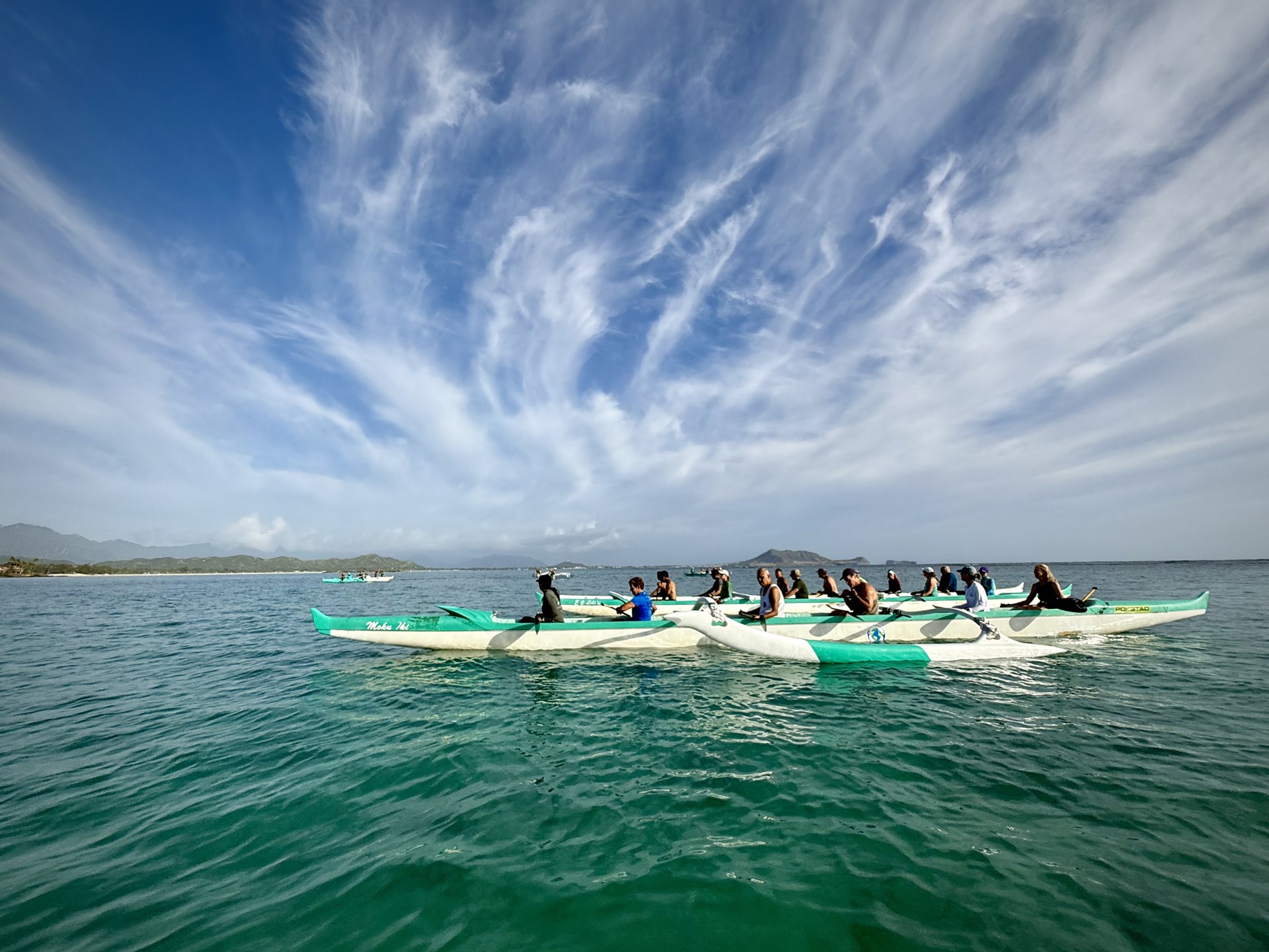 An outrigger canoe crew paddling beneath wispy clouds